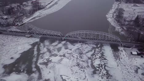 Drone-Volando-Alto-Sobre-El-Puente-Giratorio-Con-Grandes-Trozos-De-Hielo-En-Un-Río-Nevado-Durante-Una-Tormenta-De-Invierno