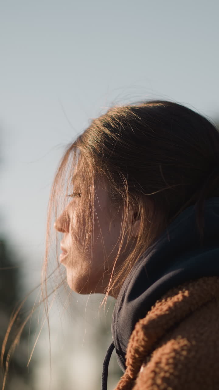 un primer plano de una chica con un abrigo marrón, con el cabello cubriendo parcialmente su cara. parece profundamente infeliz y perdida en sus pensamientos. el fondo está suavemente borroso