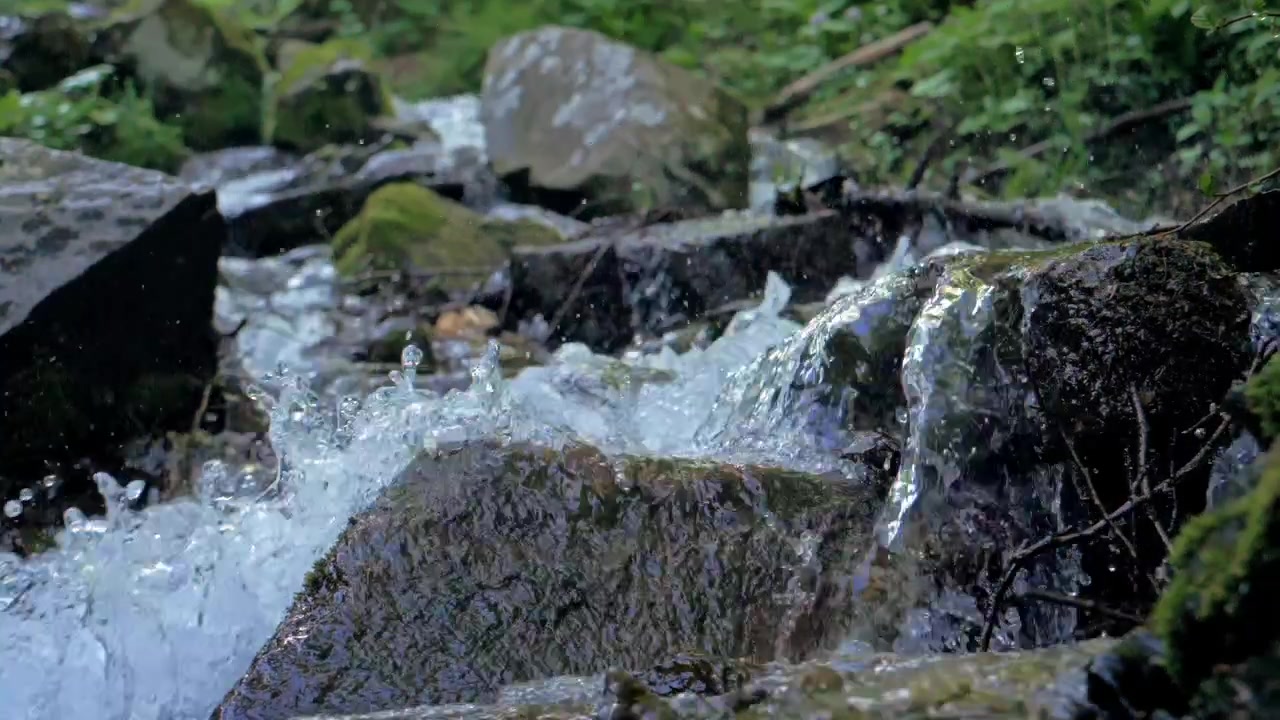Close up slow motion creek stream rushing across mossy stones with white foam bubbles small splashes and soft natural forest background texture
