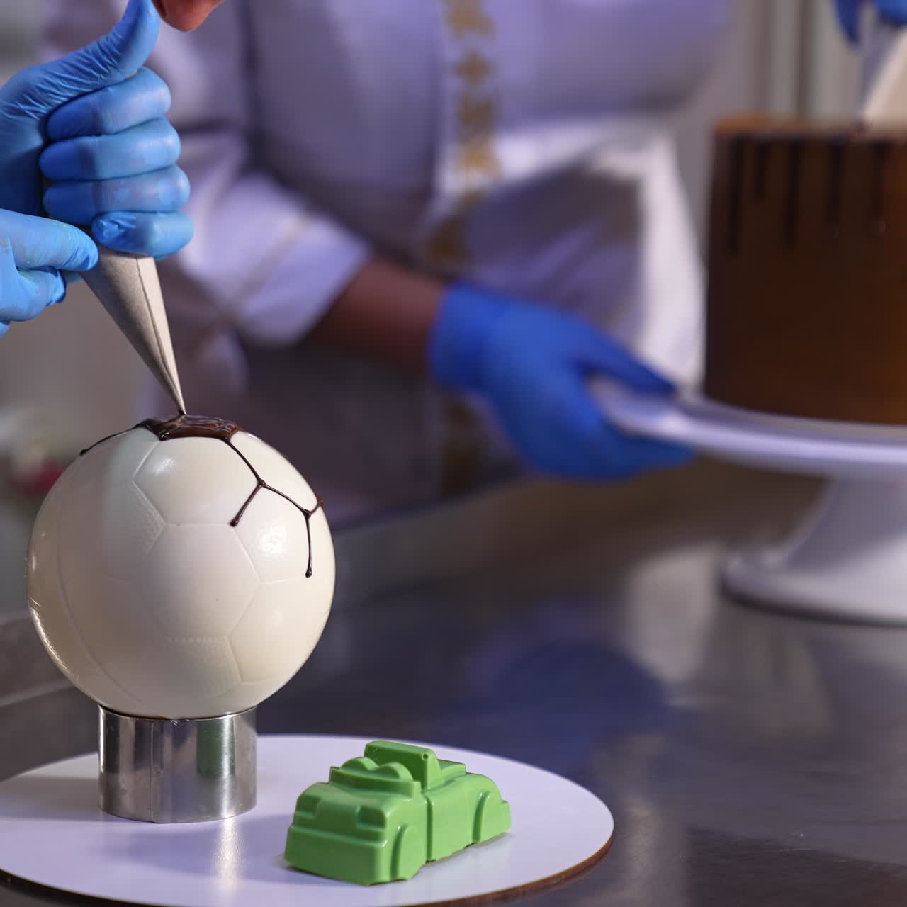 Confectioners decorating cakes in the confectionary. Two cooks working with sweets at the metal table. Blurred backdrop