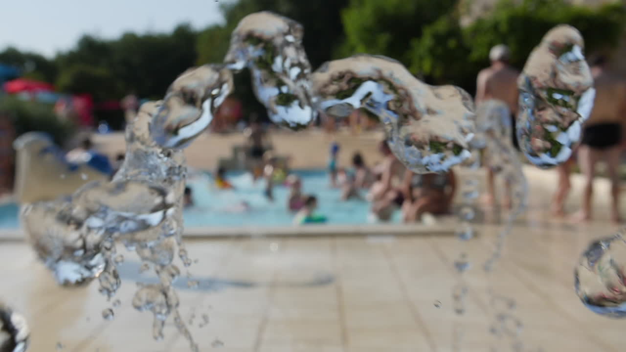 fuente de agua en cámara lenta en un campamento, la gente se enfría en un fondo de la piscina