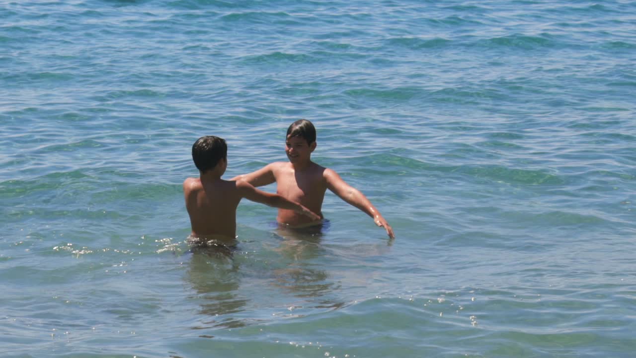 2명의 백인 형제들이 바가에서 서로 물을 뿌리며 손을 흔들고 놀고 있는 중간 속도 속도 영상입니다.