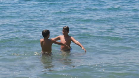 medium 100fps slow motion footage of two caucasian brothers waving their hands in the air, playing at the seashore, splashing each other with water