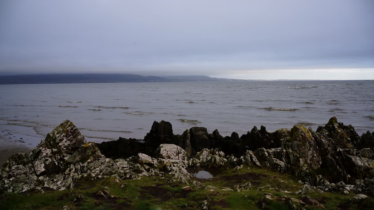 vista estática de las rocas y el océano, las olas rompiendo en la playa de arena en dundalk, irlanda