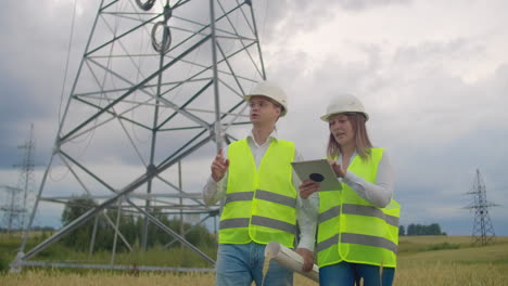 Power-lines-man-and-woman-engineers-with-a-tablet-in-their-hands-check-the-progress-of-the-installation-of-new-towers-and-analyze-the-network