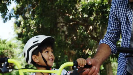 father and son standing with bicycle in park