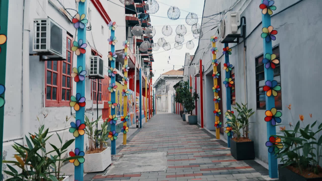 Un vicolo storico stretto è splendidamente decorato con file verticali di vivaci girandole di fiori e globi di lanterne appese.