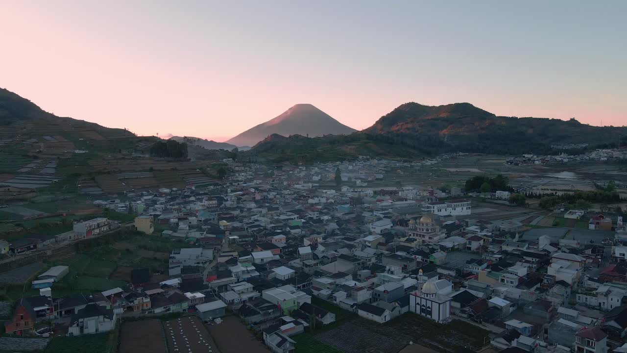 vista aérea del hermoso amanecer en el campo de indonesia con vista a la construcción de la aldea y la cordillera - toma de avión no tripulado de la meseta de dieng