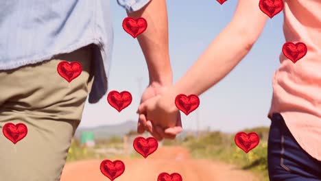 Multiple-heart-balloons-floating-against-mid-section-of-couple-holding-hands