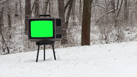 old vintage tv with green screen on chair in the forest covered by snow