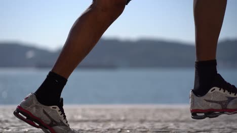 piernas de hombre atlético en zapatillas de deporte corriendo a orillas del río