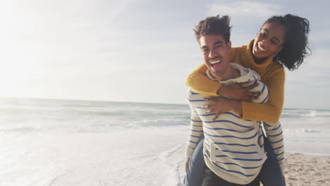 hombre hispano feliz llevando a una mujer a hombros y divirtiéndose en la playa