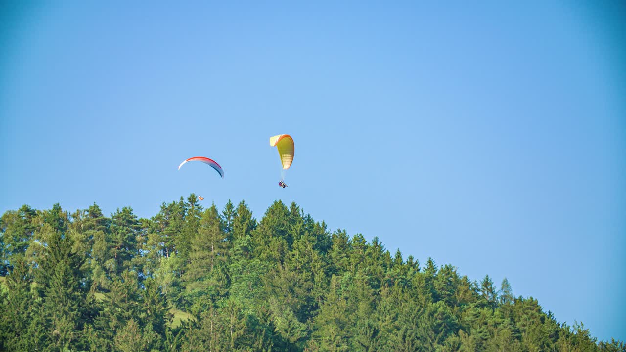 two people practising paragliding above forest in Slovenj Gradec. Slow motion