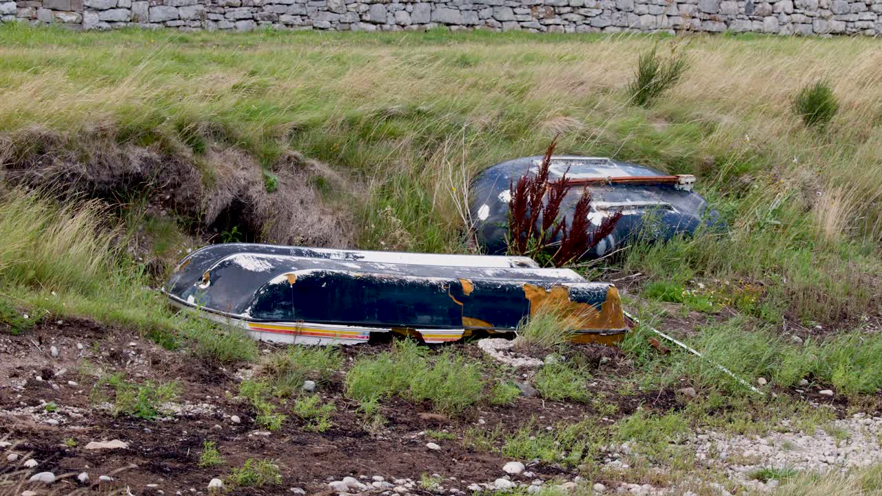 Two old, weathered boats lie unused on grassy, muddy shore under soft, natural daylight