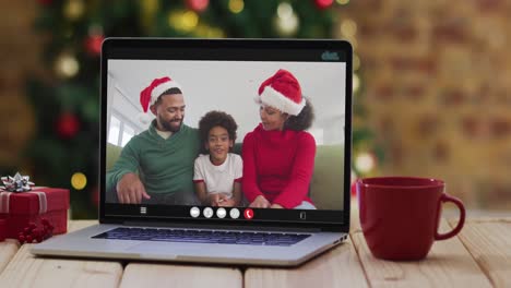 Happy-family-wearing-santa-hats-on-laptop-video-call,-with-christmas-decorations-and-tree