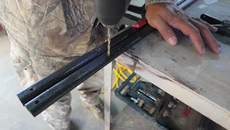 a skilled worker operates a drill, creating holes in metal strips while focused on maintaining accuracy and technique. the workshop emanates a hands-on atmosphere.