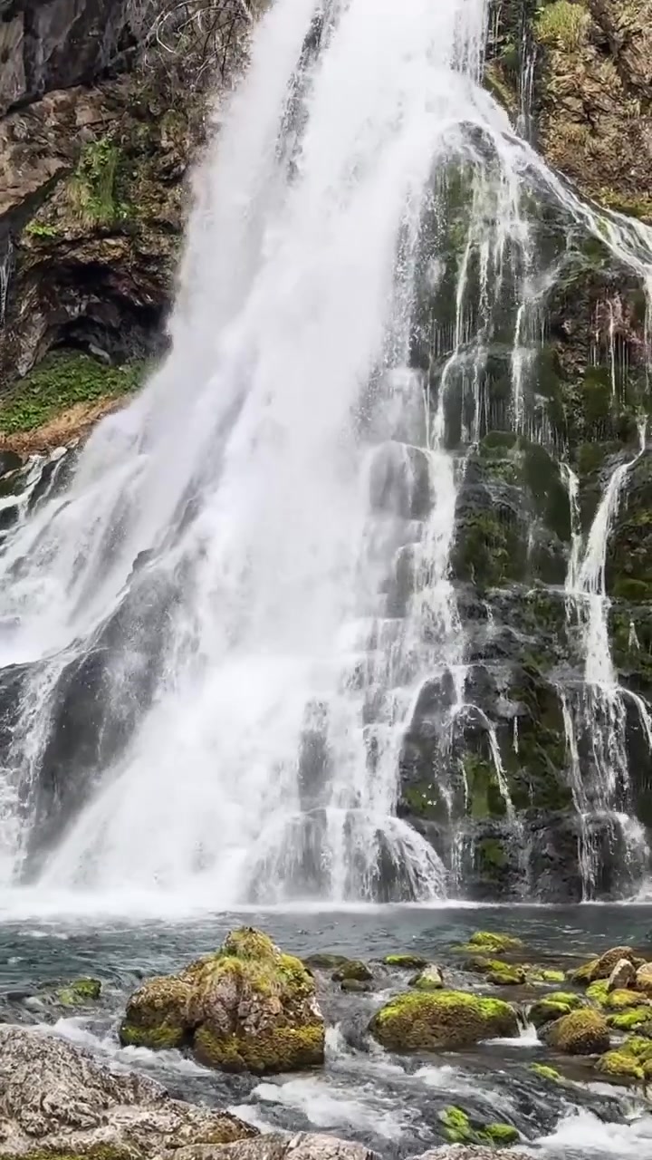 Cascata di Golling in Austria che scende a cascata su roccia scura in una pozza limpida, con massi chiari, muschio, spruzzi e pareti della gola boscose