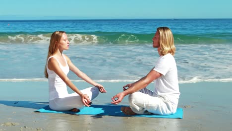 couple performing yoga at beach