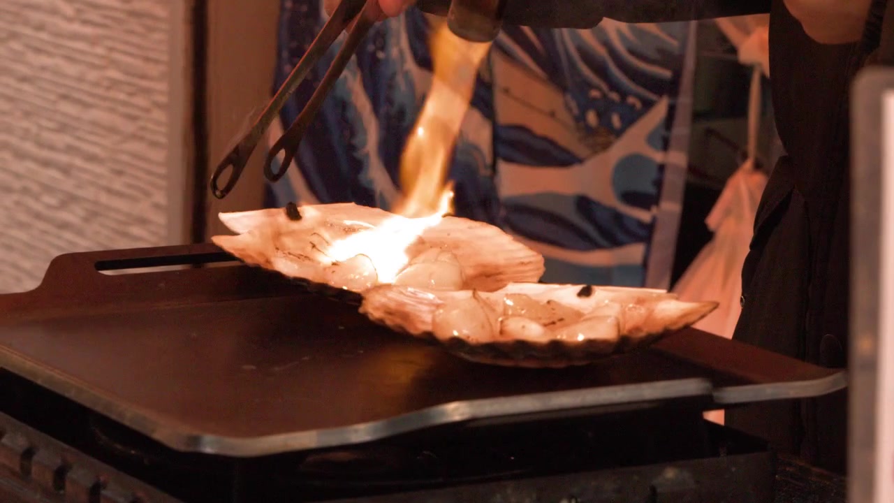 Close-up shot of a street food vendor searing fresh scallops with a blowtorch flame