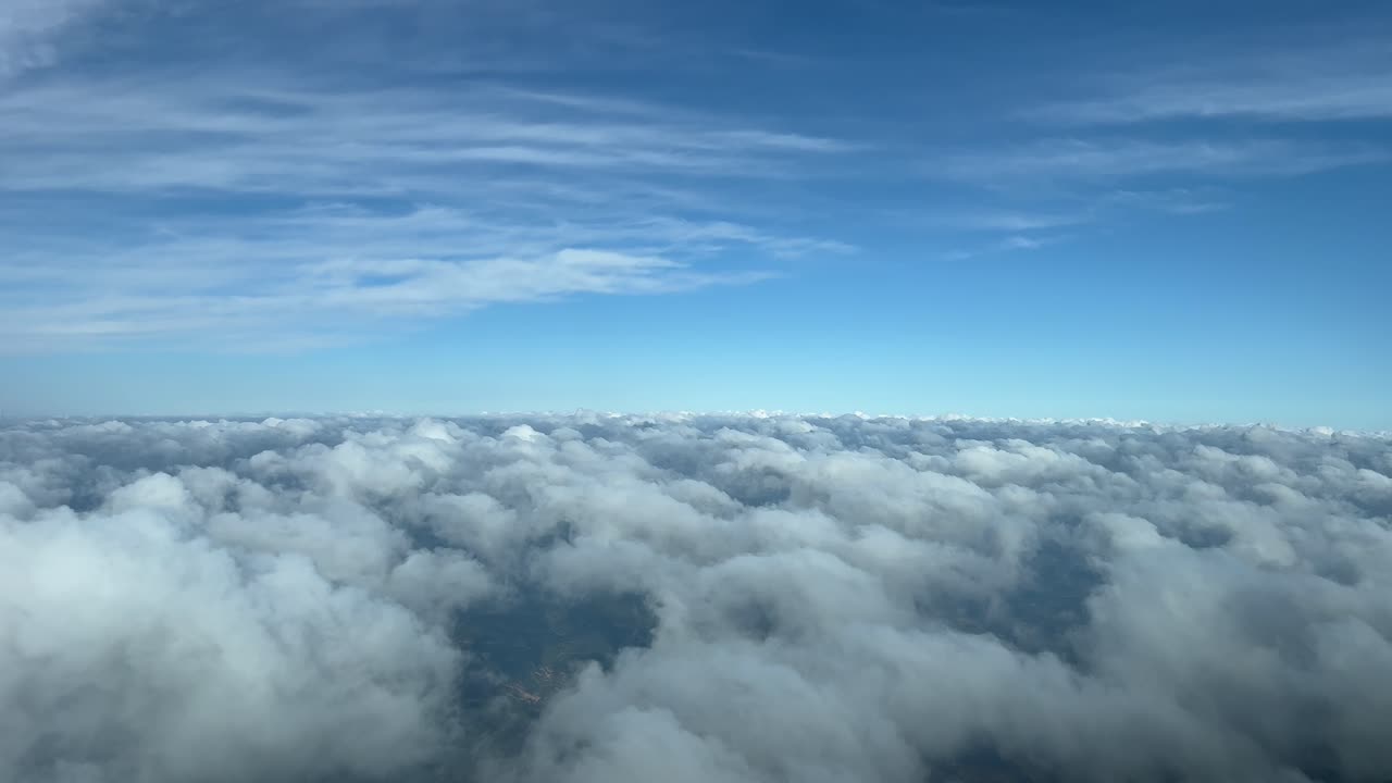 Flot udsigt fra et jetcockpit, fra pilotens synsvinkel, der overflyver et lag af små cumulusskyer
