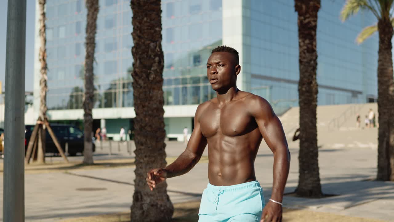 Shirtless muscular man walking among palm trees