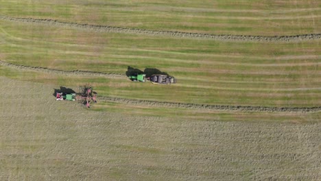 Vista-Aérea-De-Arriba-Hacia-Abajo,-El-Tractor-Con-Henificador-Crea-Una-Fila-Para-Producir-Fardos-De-Silo