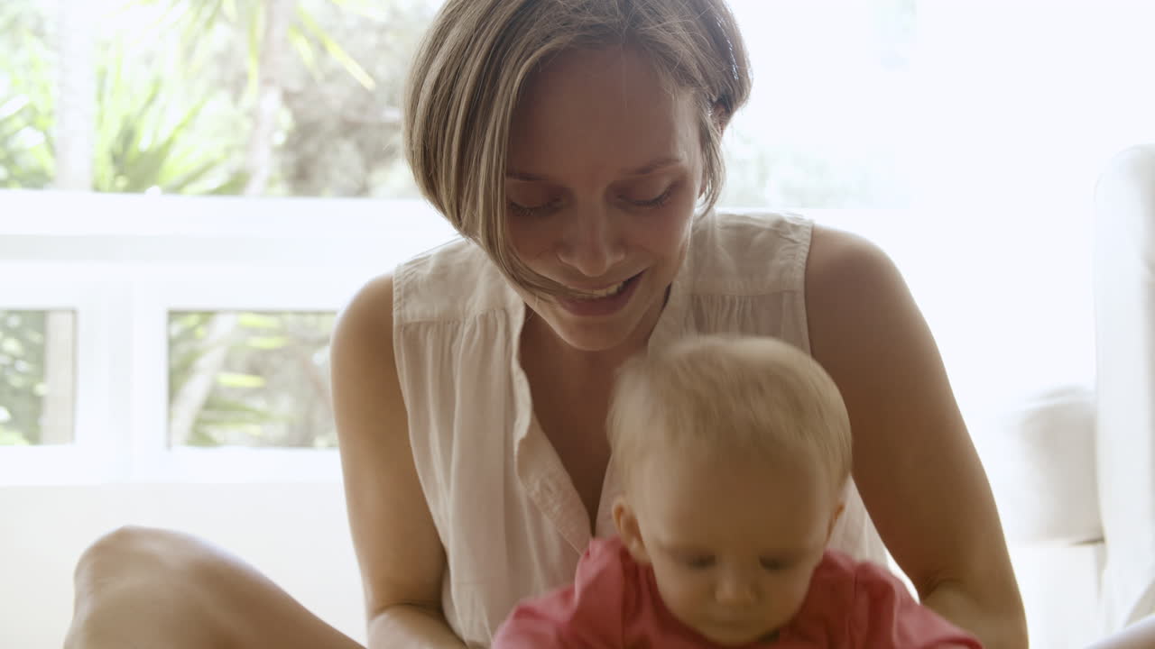 madre caucásica sosteniendo a una niña, jugando con el bebé y sonriendo