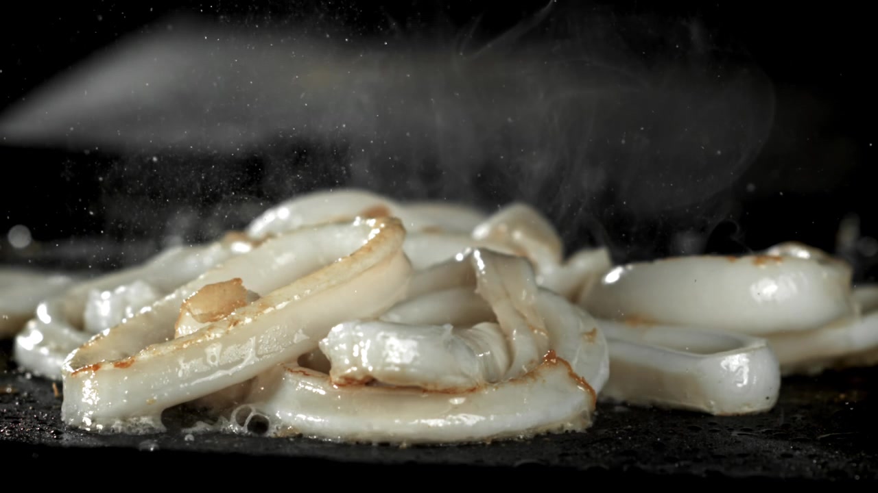 Anelli di calamari sfrigolanti che friggono su una superficie calda
