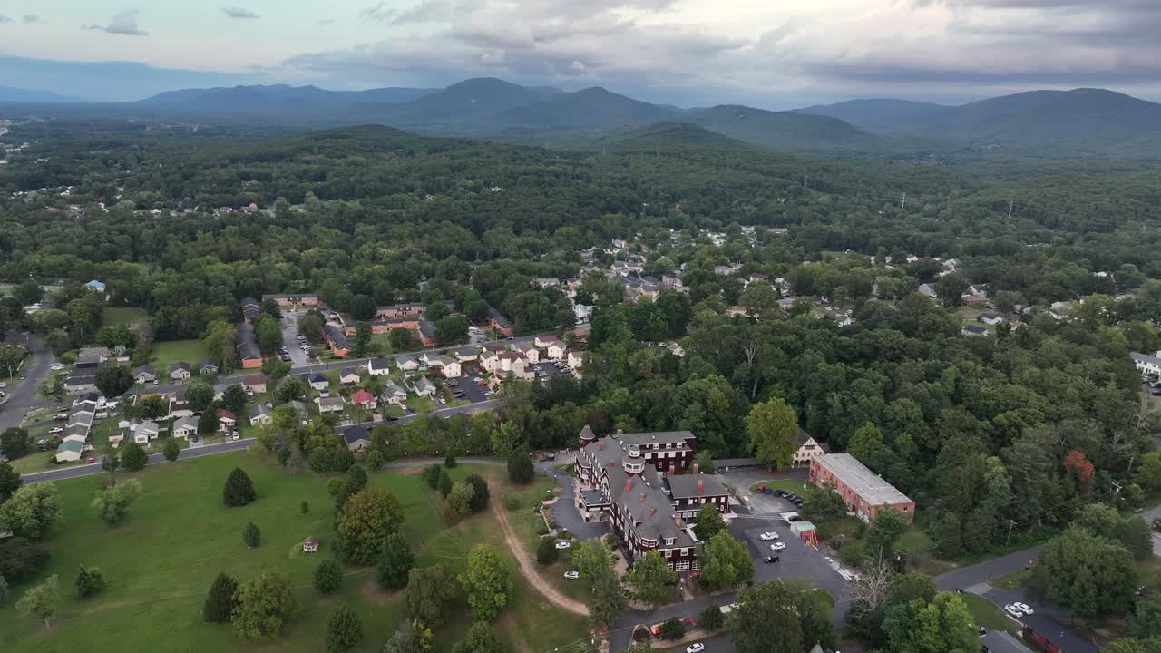 American suburb neighborhood and school campus in suburb of town. Cloudy summer day with green trees. Houses and homes in district. Blue ridge mountains in distance. Aerial flyover shot
