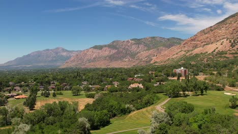 a drone shot of a golf course next to some mountains and located in the suburbs in the summer time