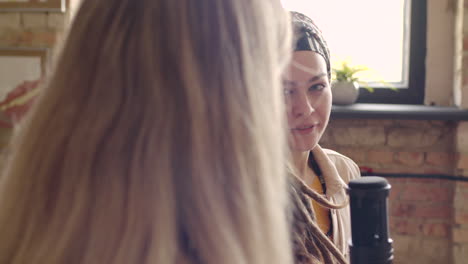 Close-Up-View-Of-Two-Women-Recording-A-Podcast-Talking-Into-A-Microphone-Sitting-On-Sofa-1