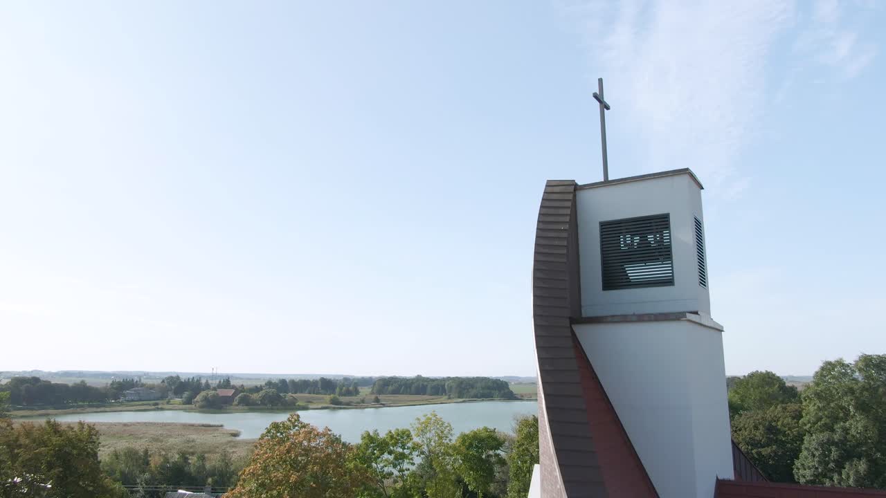 Drone ascending view from beautiful red roofed church and revealing lake, flatland with trees and bright blue sky of Lithuania, aerial drone shot