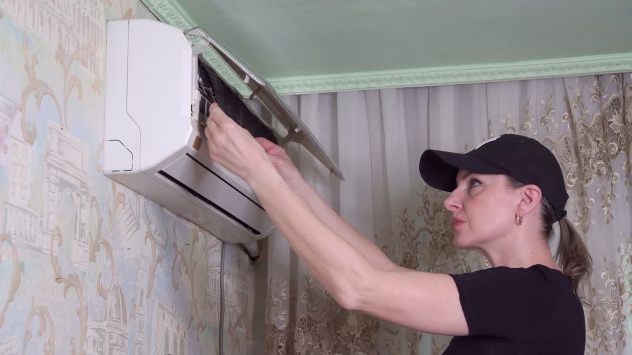 Air conditioner repairman removes air filter to clean it of dust.