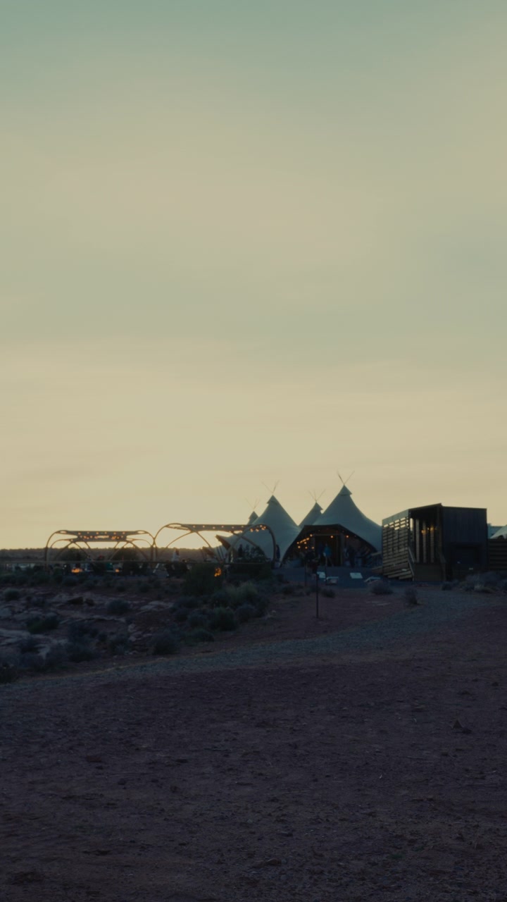 Vertical view of a desert glamping venue at dusk, teepee tents beneath open sky