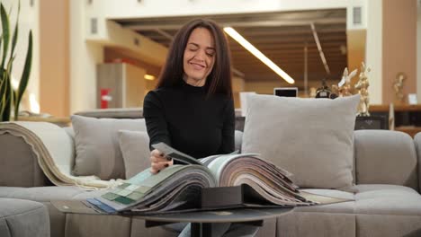 woman sitting on modern sofa browsing home interior catalog in furniture showroom a woman comfortably sits on a stylish sofa inside a furniture store flipping through a home interior magazine to find ideas for renovation and design