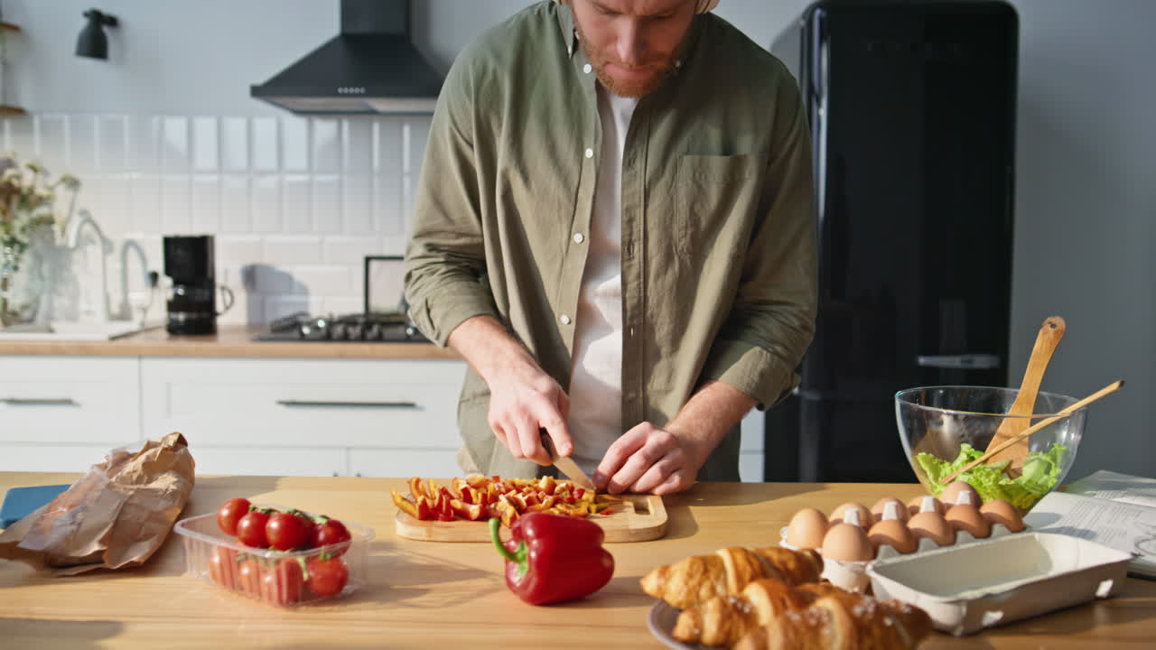 Dancing man slicing vegetables at kitchen countertop in earphones closeup