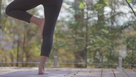 a lower body shot of a a woman in a tree pose yoga stance on an outdoor balcony in the country