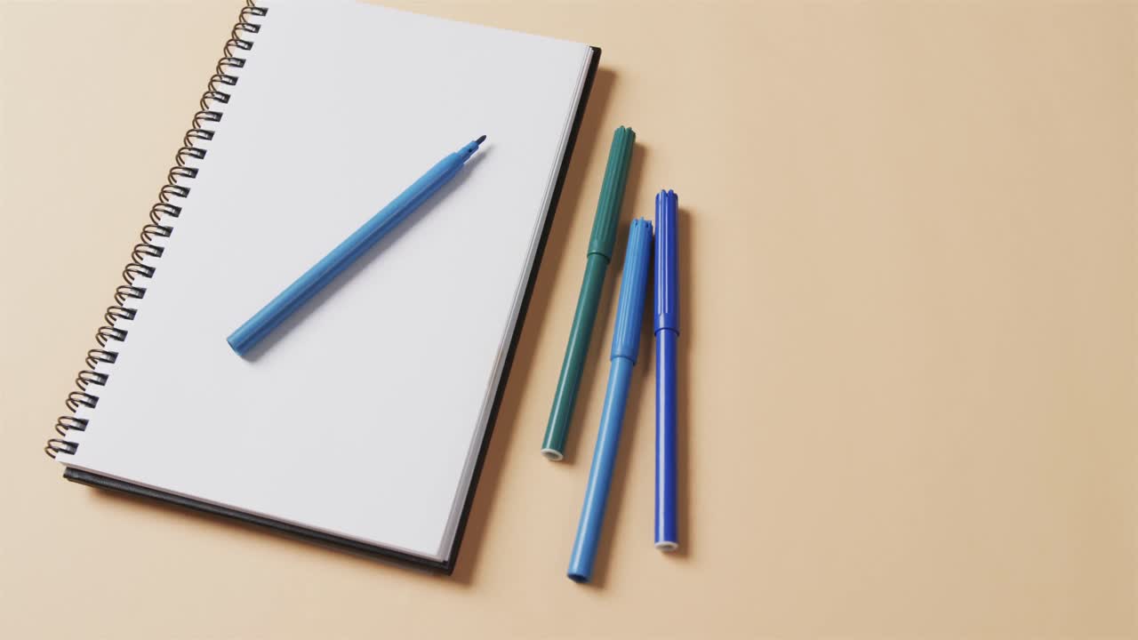 베이지색 배경에 복사 공간을 가진 노트북과 함께 파란색 마커의 클로즈업, 느린 움직임