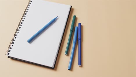 close up of blue markers with notebook with copy space on beige background, in slow motion