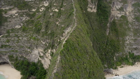 fly by along the ridge with a pathway down to kelingking beach next to huge steep cliff, nusa penida, bali, indonesia