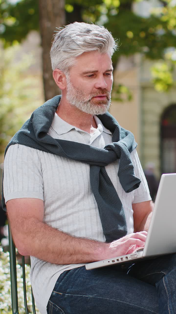 Middleaged man opens laptop start working sends messages sitting on chair in urban city street