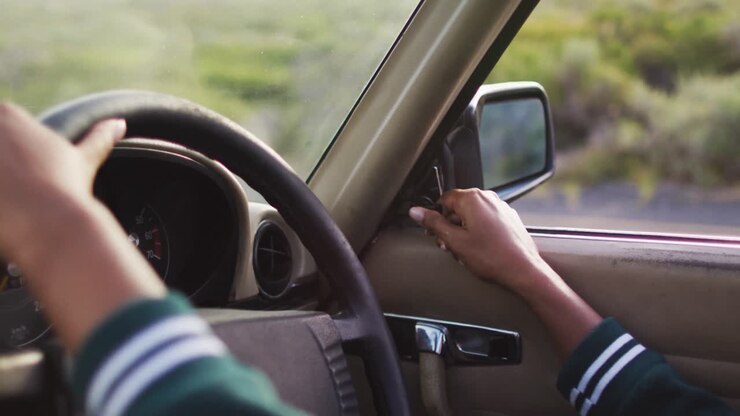 Busto di donna che regola lo specchietto retrovisore laterale mentre guida lungo una strada di campagna in un'auto decappottabile