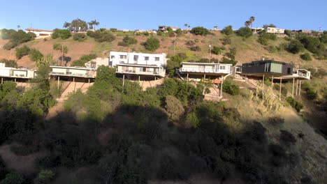 Aerial-flyby-of-homes-on-stilts-hanging-off-cliffs-of-a-mountain-overlooking-a-valley-city