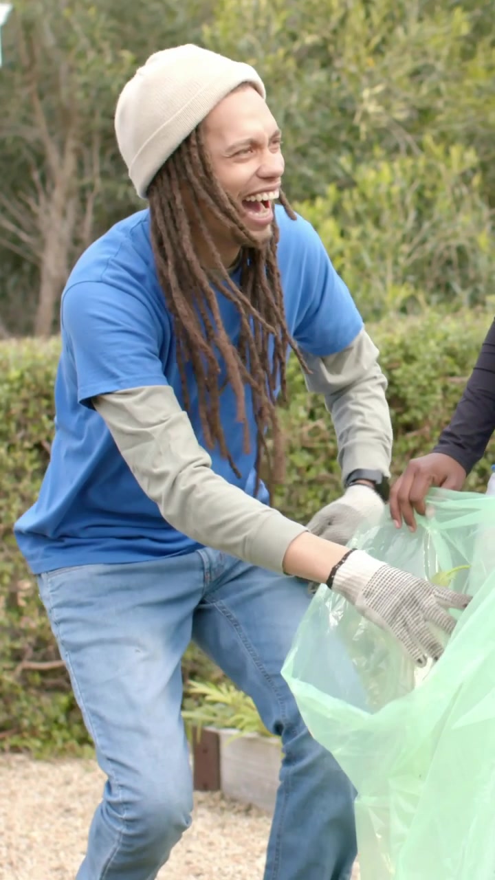 Vertical video: Starting, man with gloves pulling plants from raised bed into green bag for cleanup