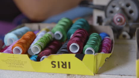 coloridos carretes de hilo temblando junto a una máquina de coser mientras una mujer borda en el fondo