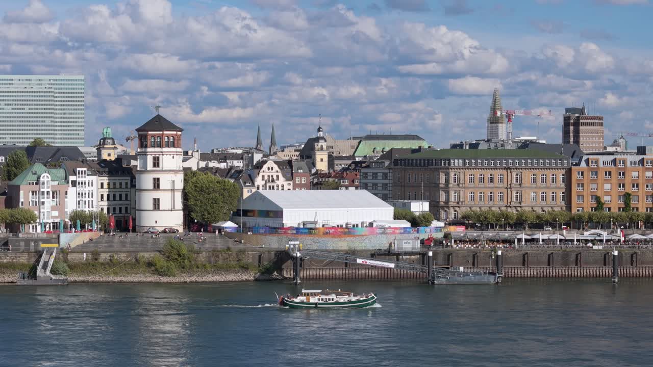 A small riverboat passes by D&uuml;sseldorf on the Rhine under a cloudy sky