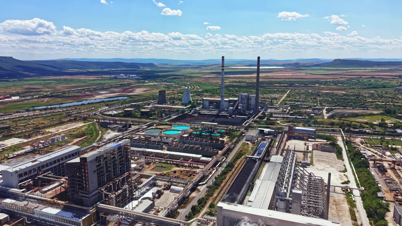 Sito industriale con centrale elettrica e paesaggio sullo sfondo durante il giorno con cielo blu e nuvole