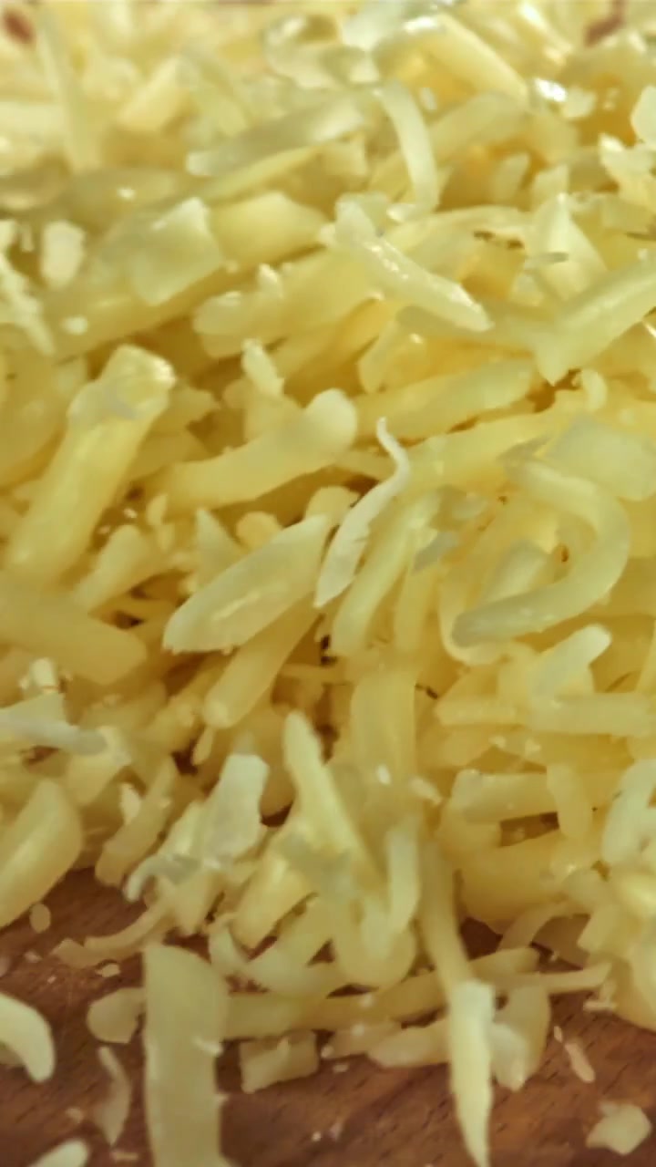Formaggio fresco grattugiato che cade su un tagliere di legno