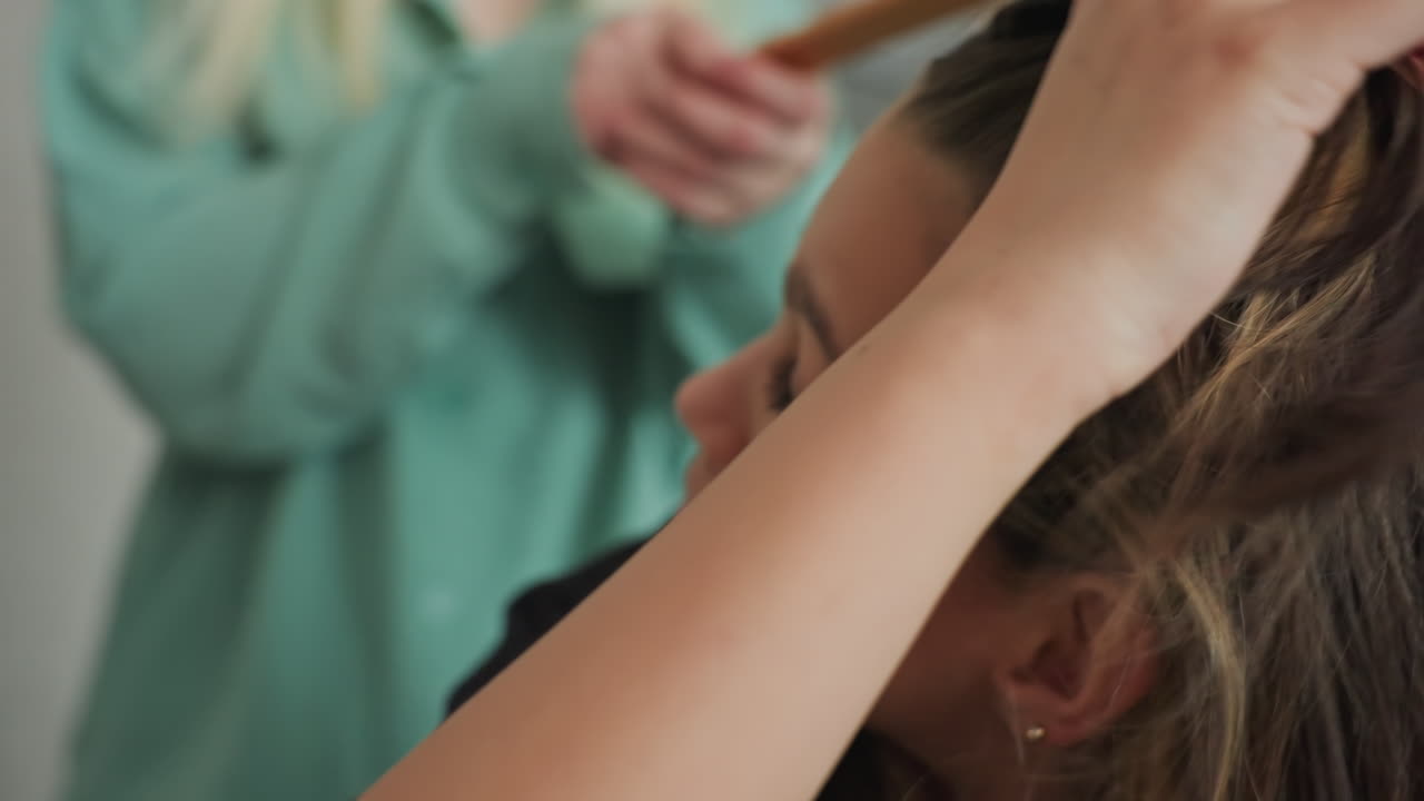 young women in kitchen use mixing bowl as hat and spoon to playfully tap head while laughing near snack bag and potted plant for light hearted sibling bond around cozy table laden with snack
