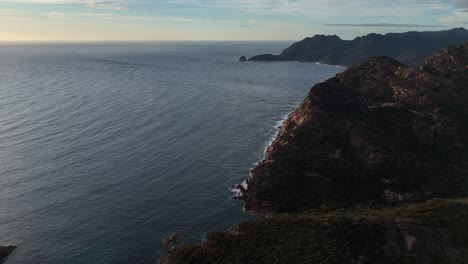 coles bay conservation area with freycinet mountain in tasmania, australia during golden sunrise. aerial wide shot.